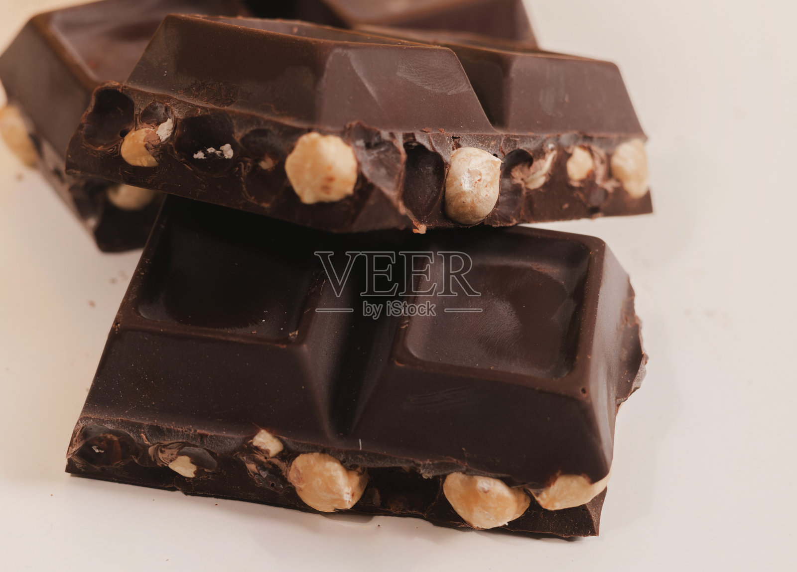 白色背景上的破碎黑巧克力棒，夹杂着榛子，闪耀的金色背景。奢华甜点的俯视图，巧克力块叠放在一起。盒子上留有空白空间供文字使用。照片摄影图片