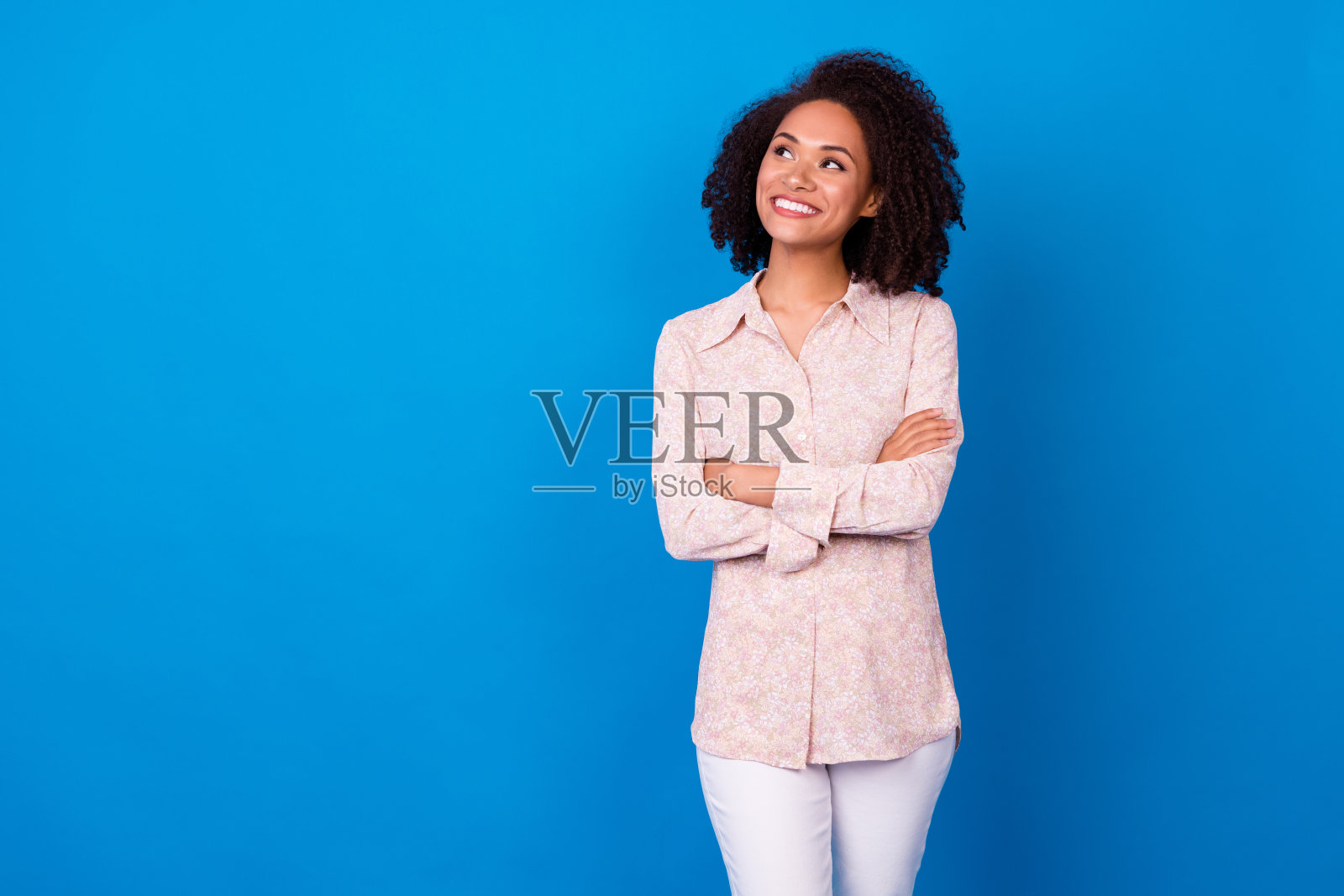 思考的快乐女孩双手交叉，凝视空旷的空间，进行头脑风暴，背景为蓝色。照片摄影图片