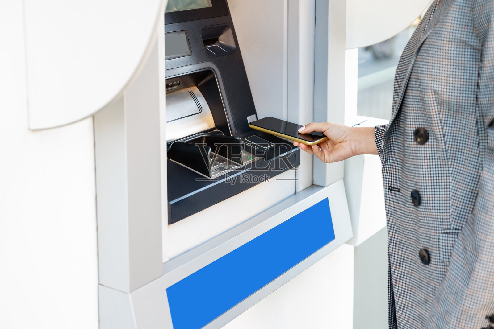 在自动取款机上使用智能手机进行现金提取的人。照片摄影图片