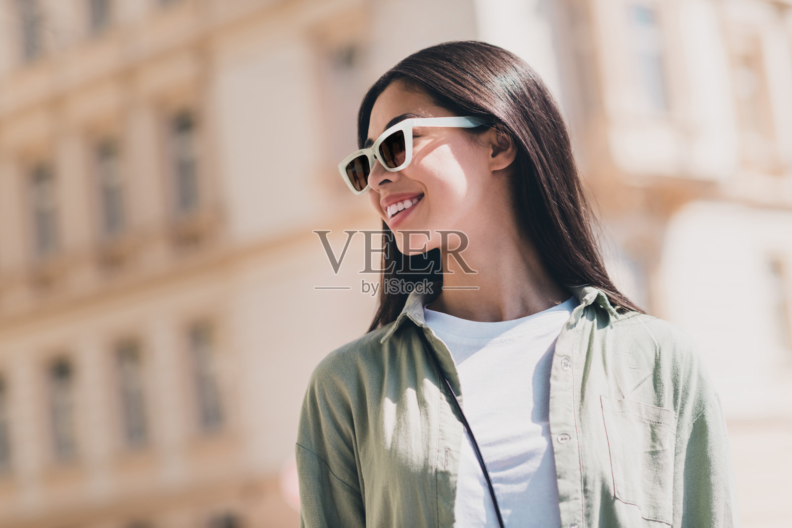 穿着绿色服装、戴着深色眼镜的漂亮快乐女友在城市街道上享受阳光天气购物。照片摄影图片