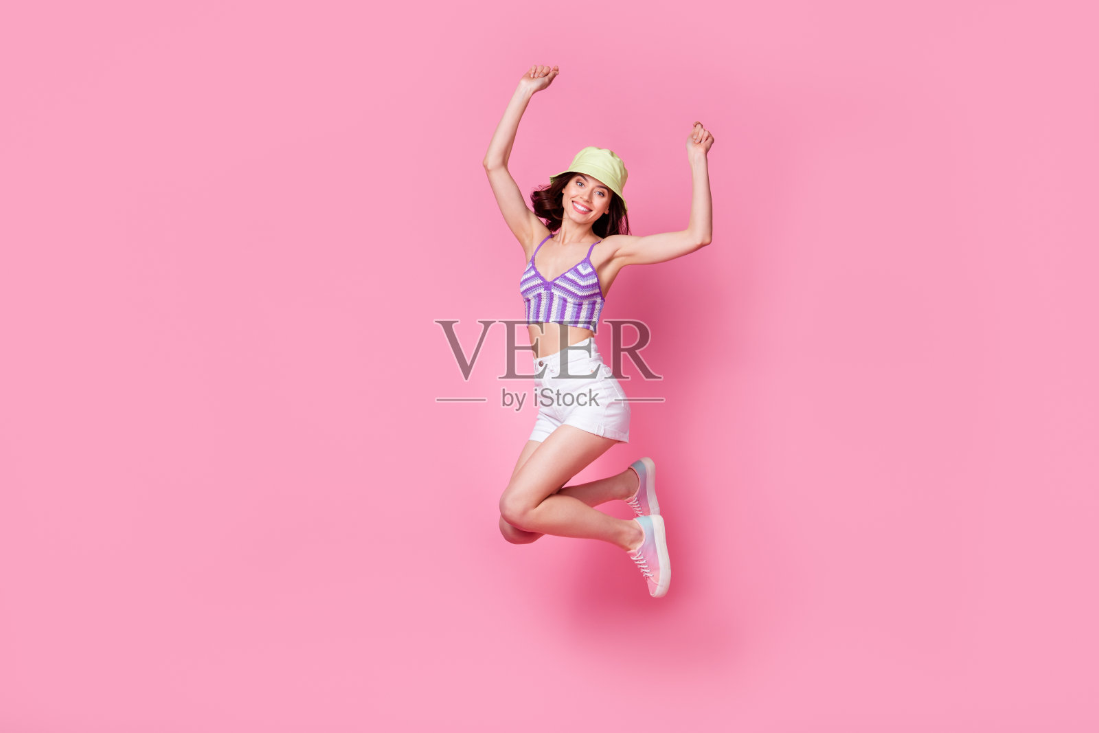 全身照的无忧无虑的女士在梦幻休闲中跳跃，双拳高举，背景为柔和的色彩。照片摄影图片