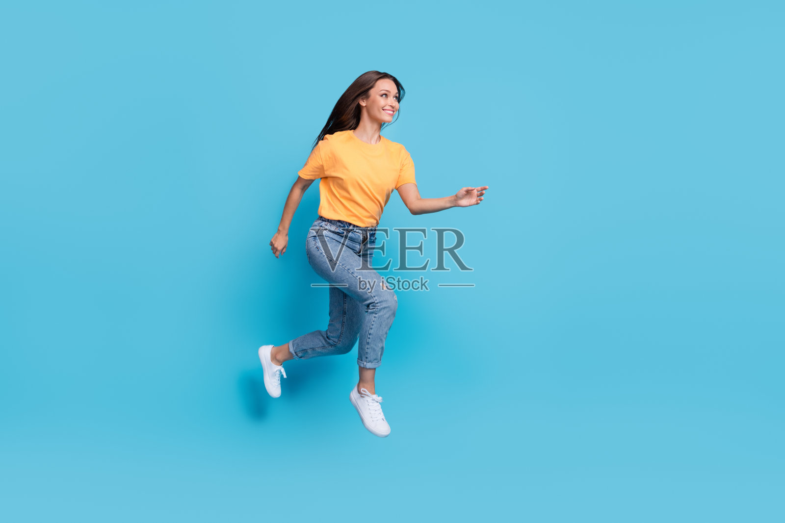 穿着黄色T恤的闪亮甜美女孩在空旷的蓝色背景下高高跳起，快速奔跑的全身照片照片摄影图片