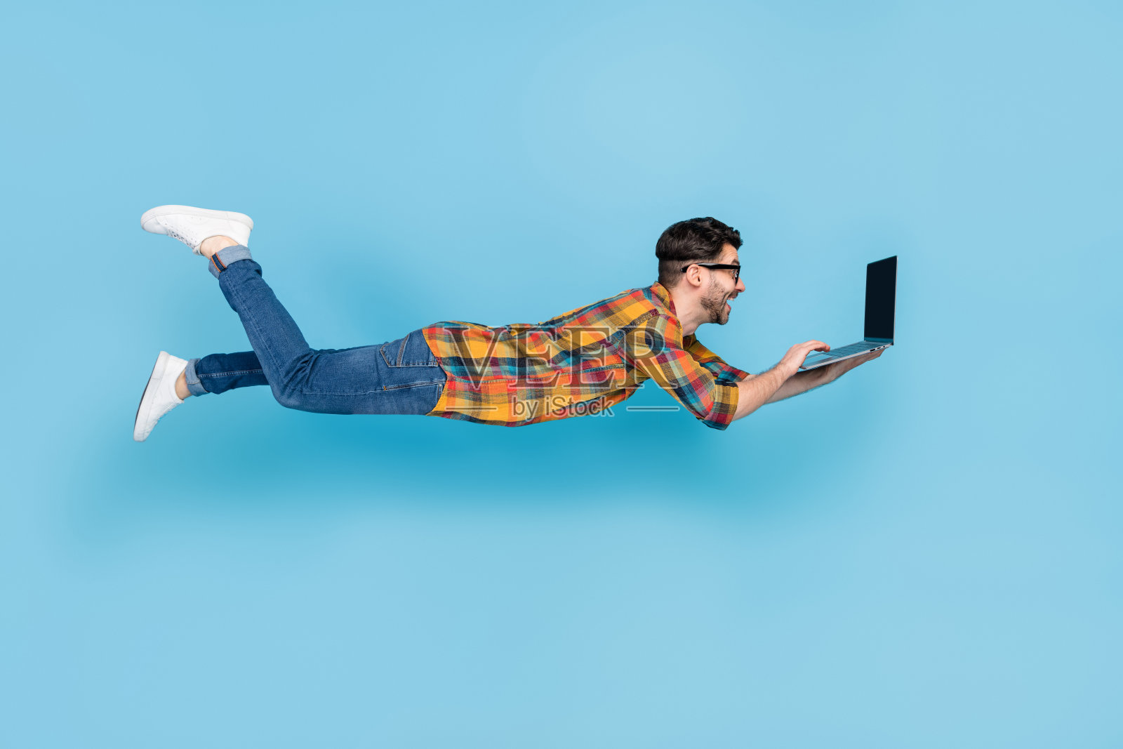 在蓝色背景下，飞行的人全身侧面照，使用笔记本电脑写电子邮件。照片摄影图片