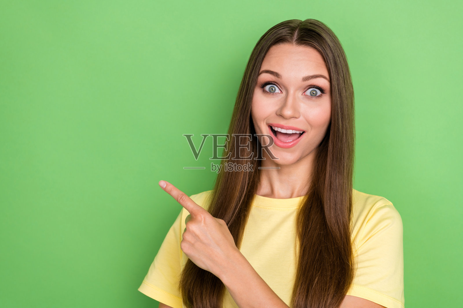 穿着黄色T恤的积极印象女孩，直发，指向绿色背景上的空白区域。照片摄影图片