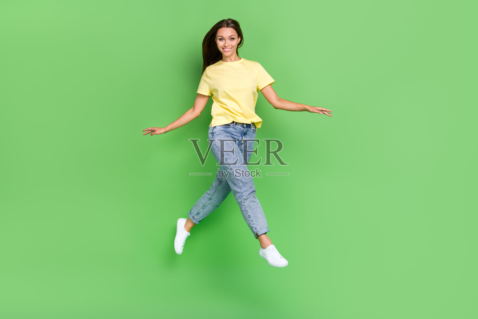 穿着时尚黄色衣服的甜美漂亮女孩在绿色背景下的空旷空间中快乐地奔跑，心情愉悦。照片摄影图片