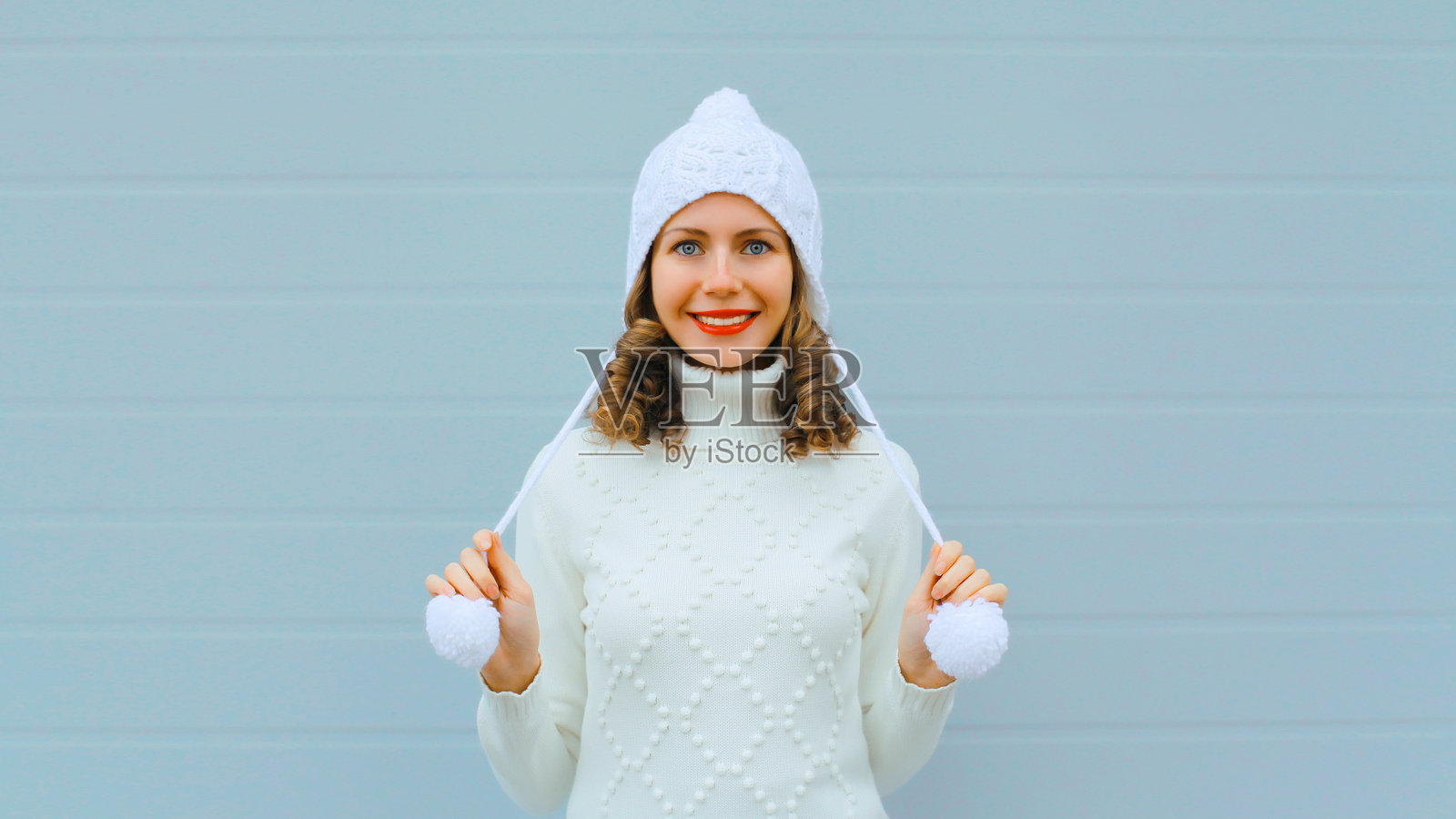 冬季肖像，快乐的年轻女性在灰色背景下微笑，戴着白色帽子和毛衣照片摄影图片