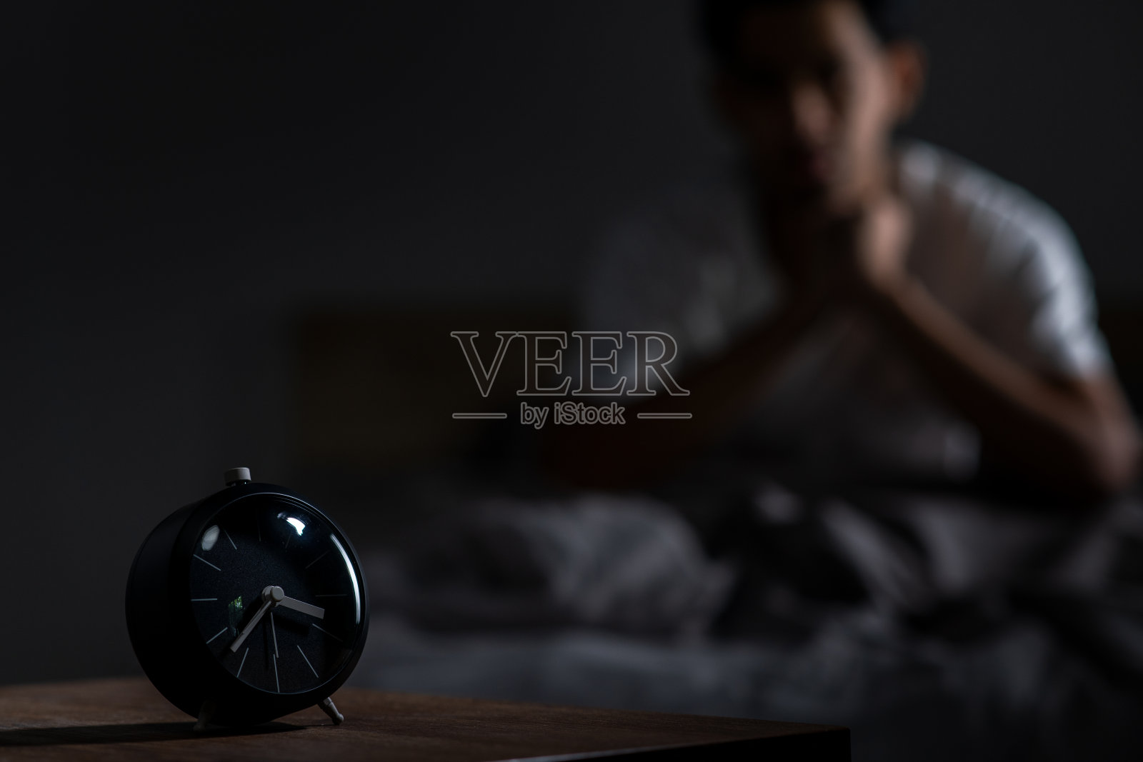 沮丧的年轻亚洲男子坐在床上，挣扎于失眠，无法入睡。照片摄影图片