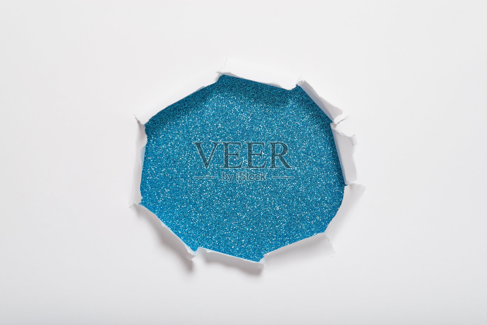 白纸中央的撕裂孔，露出蓝色闪光纹理背景。留有文本空间。照片摄影图片