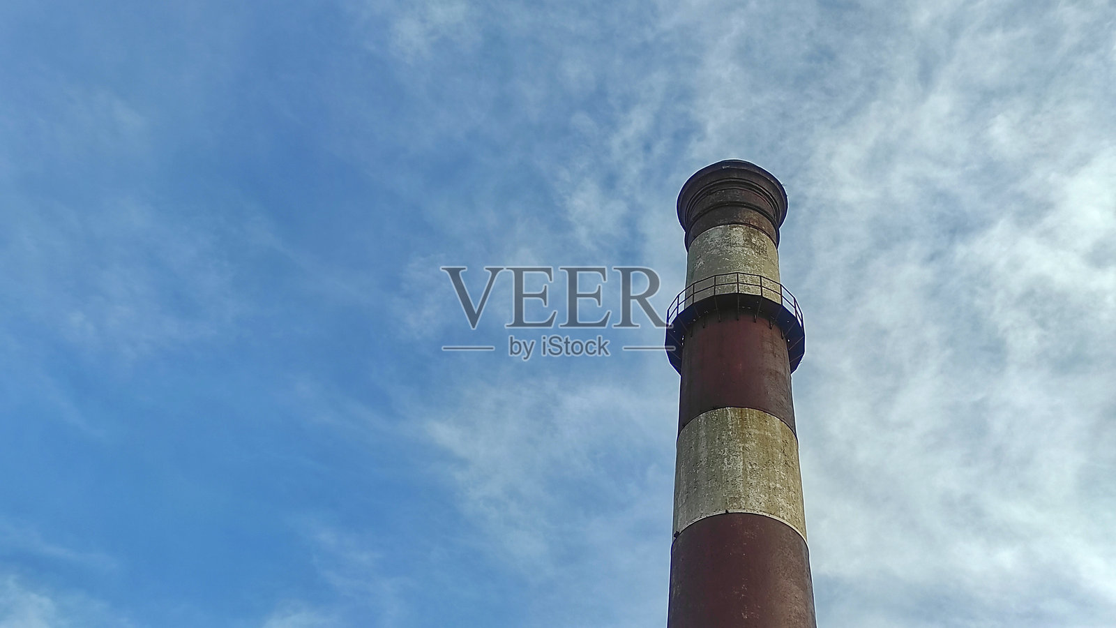 一座表面风化的老工业烟囱在明亮的蓝天下高高耸立，展现出其历史悠久和粗犷的特征。照片摄影图片