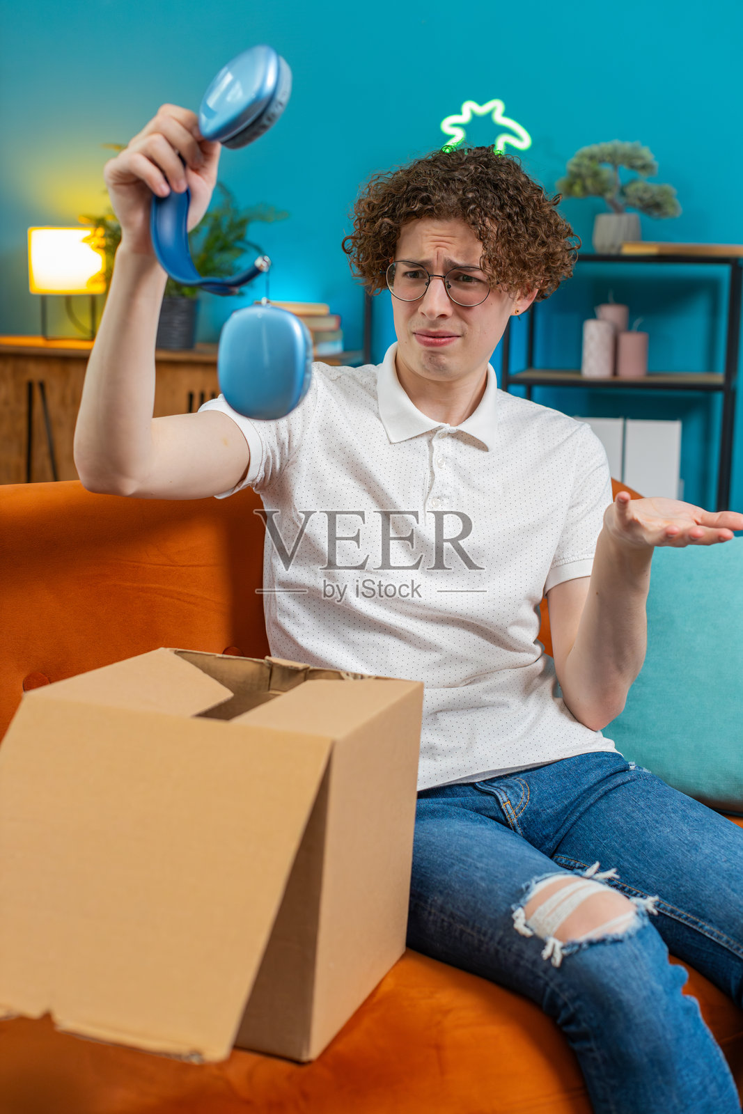 不快乐的男人在拆箱，感到对收到的损坏无线耳机不满意。照片摄影图片