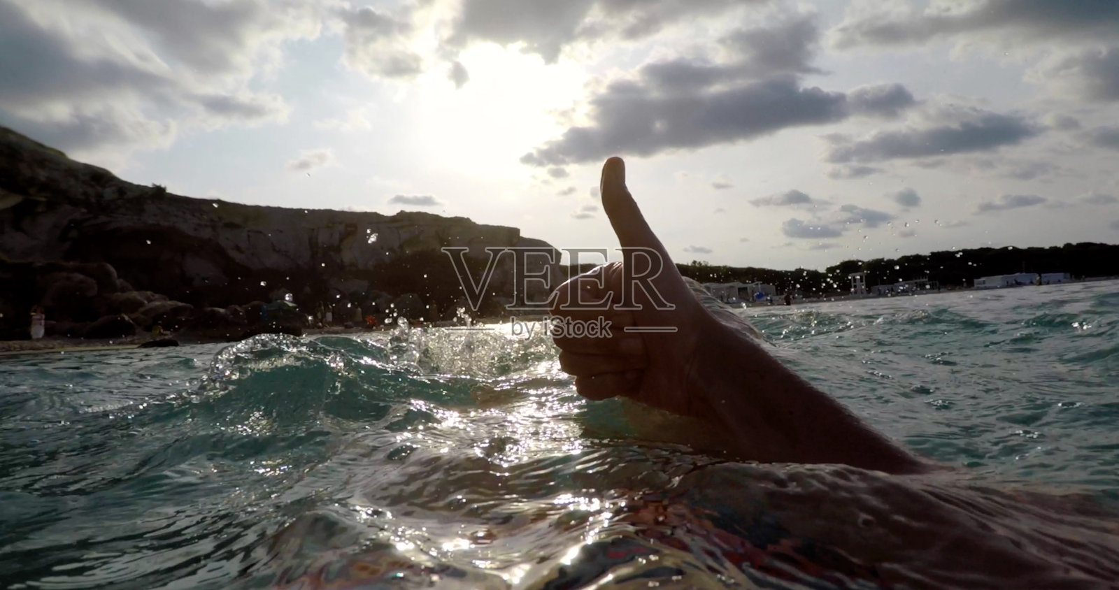 在美丽的日落下，海水中竖起大拇指的手势照片摄影图片