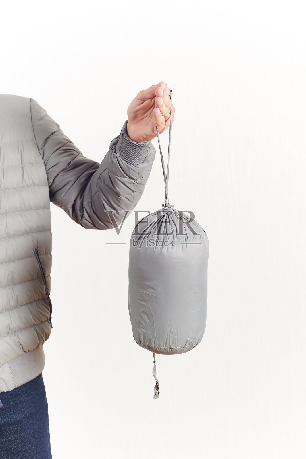 一只手握着一个灰色的压缩袋，里面装着一件可打包的紧凑型夹克或睡袋。非常适合旅行、露营和徒步爱好者。照片摄影图片