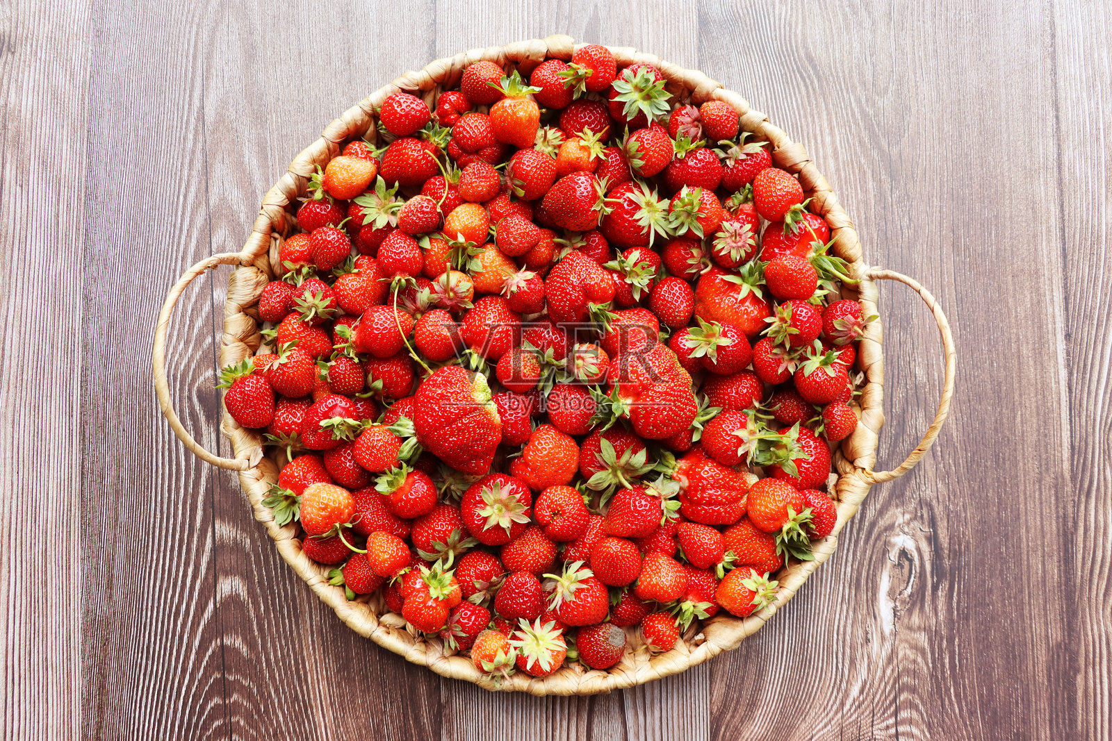 新鲜多汁的草莓在篮子里。藤制篮子里装满了刚采摘的草莓，背景是复古的木质表面。照片摄影图片