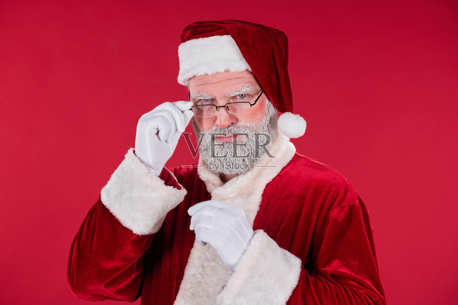 圣诞老人调整眼镜的肖像，背景为红色照片摄影图片
