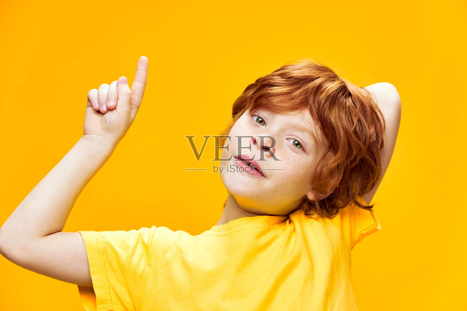 红发孩子穿着黄色T恤，用手势指向上方，食指翘起。照片摄影图片