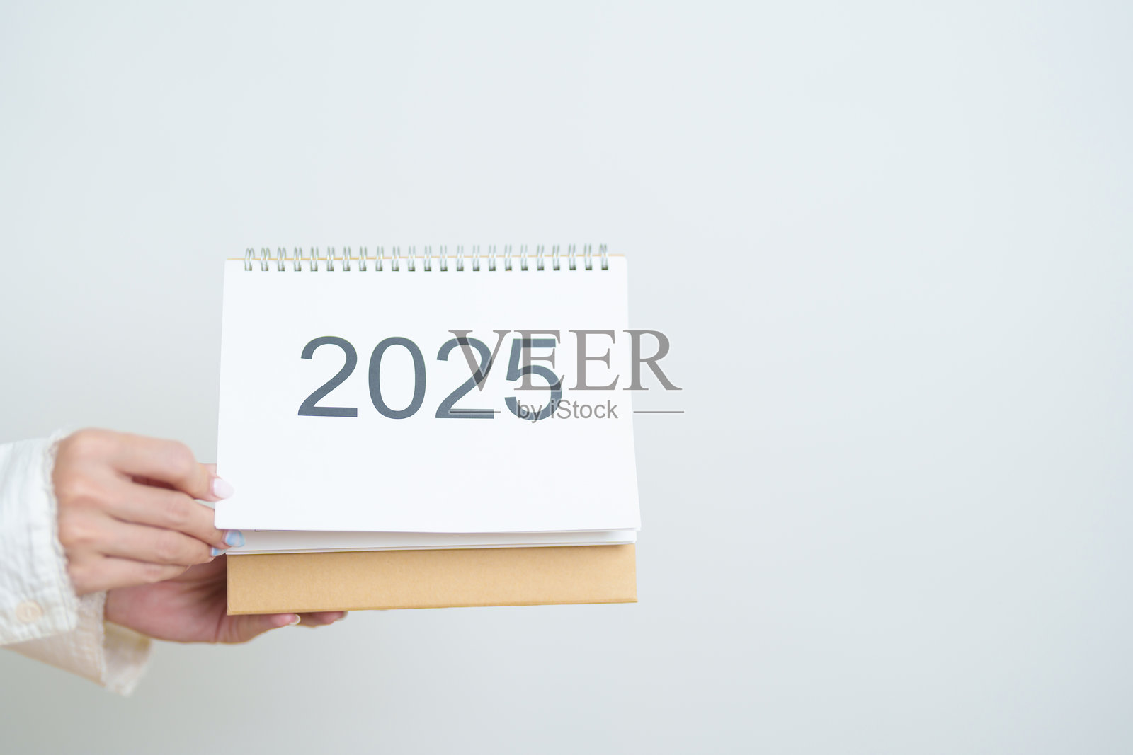 商务女性手持并更换2025年日历，放在办公室的白色桌面上。倒计时，新年快乐，决心，年终与新开始，目标计划行动概念。照片摄影图片
