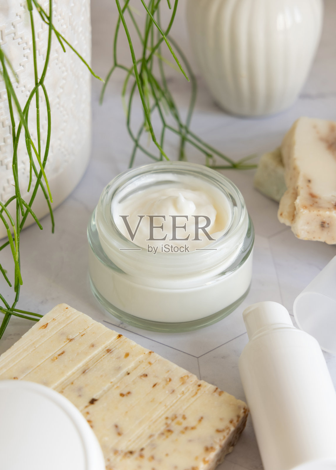 在大理石上靠近绿色植物的特写镜头中，打开的奶油罐，白色空白盖，化妆品样机。照片摄影图片