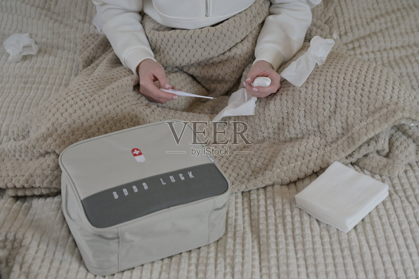 女人手持温度计和鼻用喷雾，灰色家庭急救箱放在床上照片摄影图片