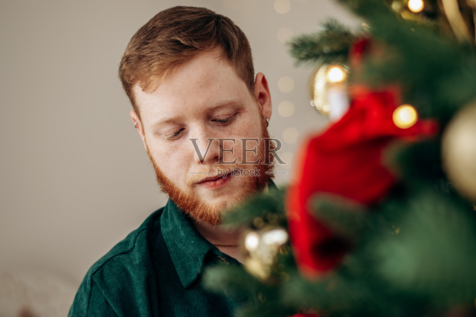 一个年轻的红发胡子男人正在家里装饰圣诞树。新年概念和圣诞概念。照片摄影图片