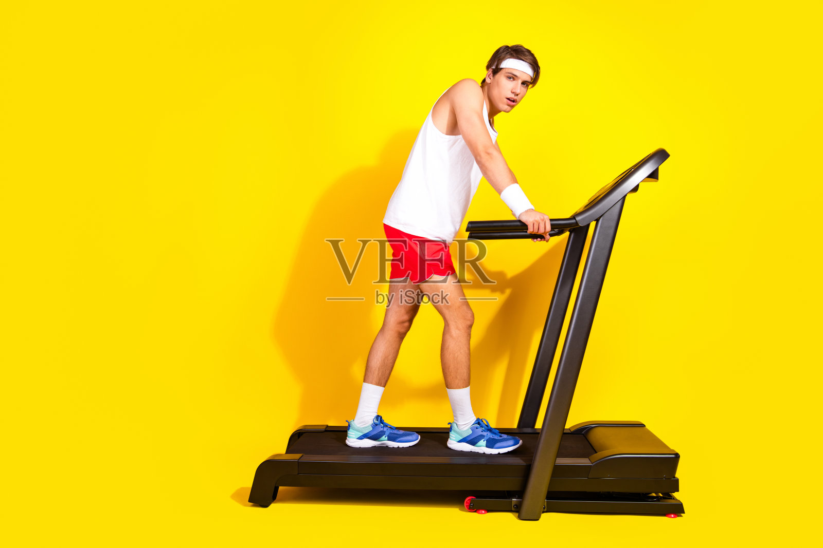 年轻运动员穿着运动服在鲜艳的黄色背景下练习跑步机照片摄影图片
