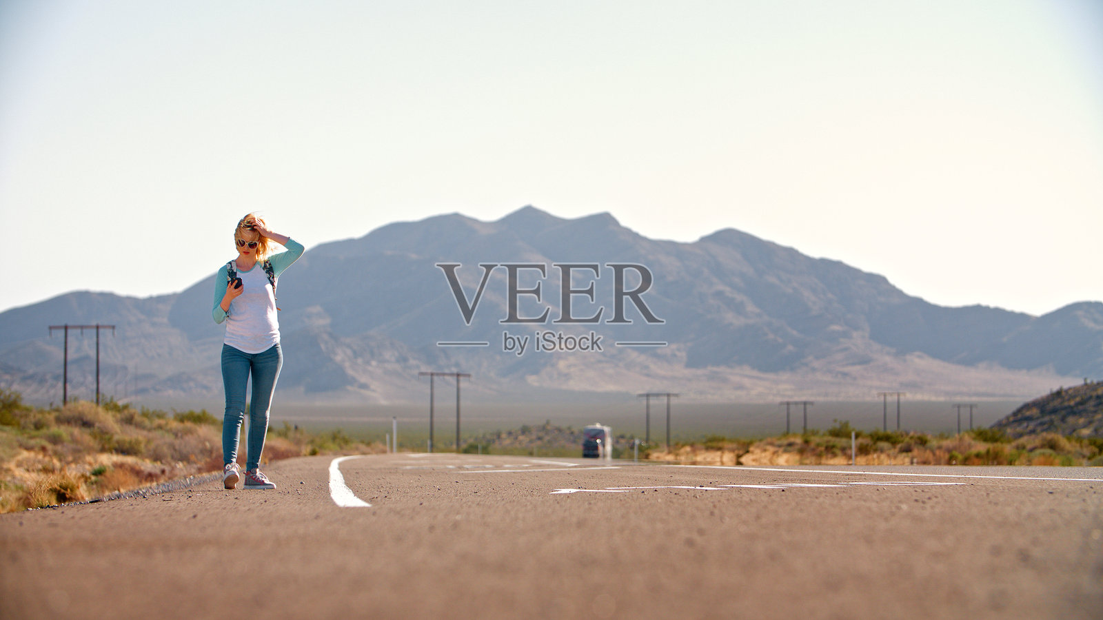 年轻女性在崎岖的乡村道路上搭便车，查看手机。照片摄影图片