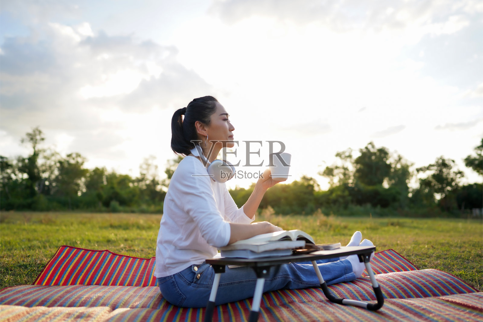 一位女性在夕阳下坐着阅读一本书，喝着咖啡。照片摄影图片
