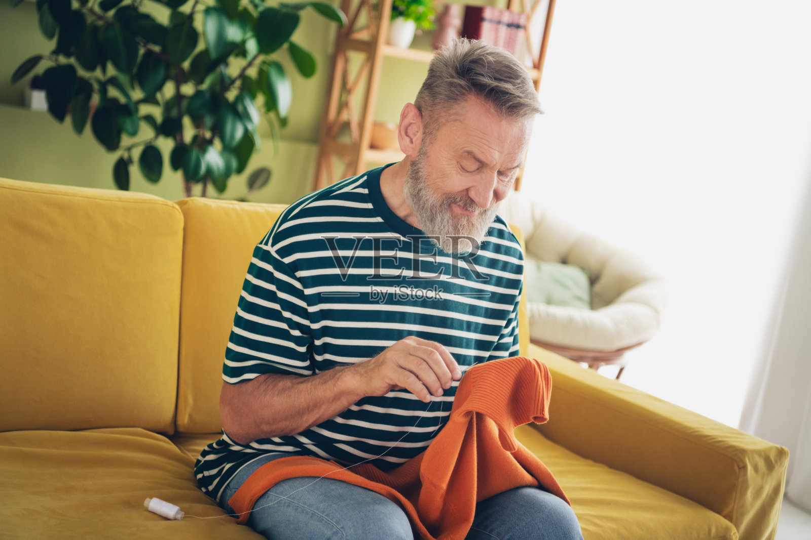 老年男子在舒适的客厅里享受轻松的周末，缝纫。照片摄影图片
