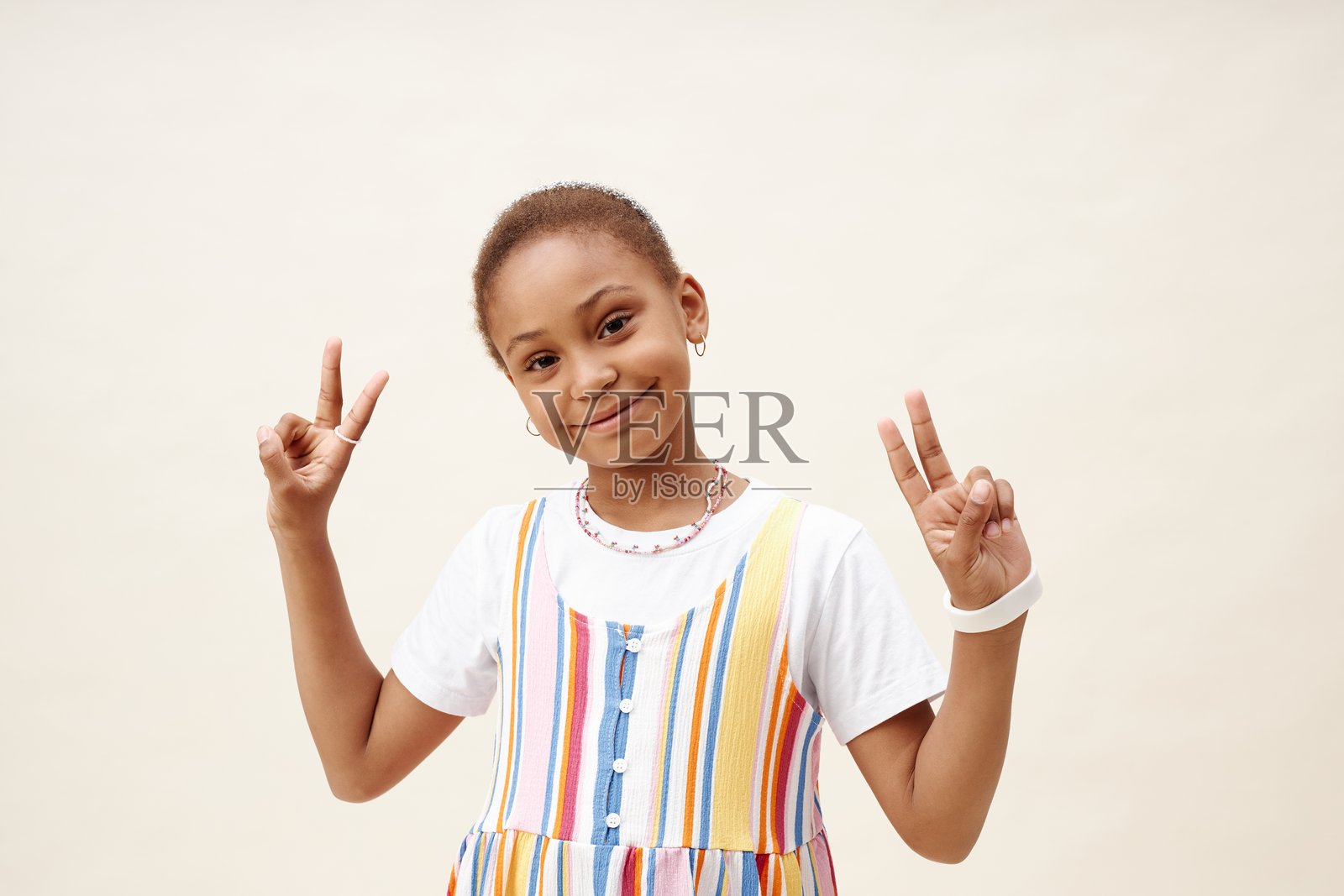 微笑的黑人女孩在摄影棚中摆姿势，双手做出V字手势照片摄影图片