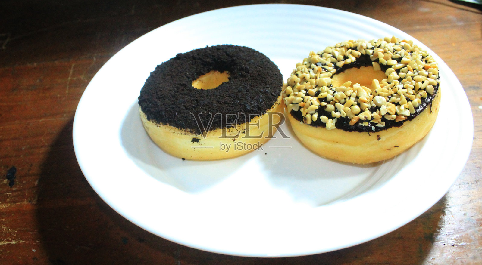 各种甜甜圈的特写镜头，白色盘子上有巧克力花生和双重巧克力。食品和饮料背景。照片摄影图片