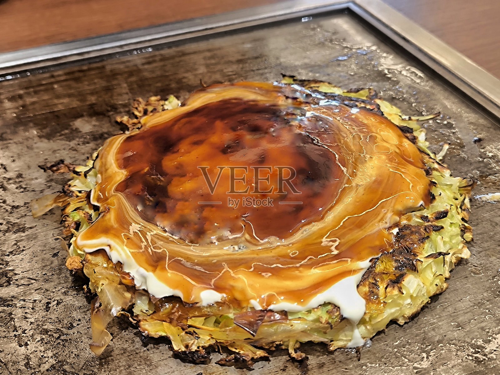 热锅上的大阪烧。这是一种美味的日本煎饼，正在铁板上烹饪。它上面淋有酱汁和美乃滋。日本铁板烧菜单。照片摄影图片