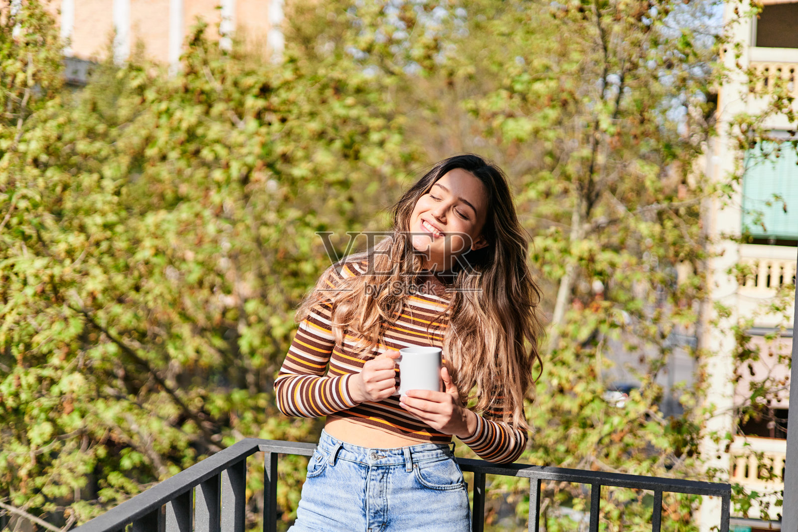年轻女子在自家阳台上微笑着喝咖啡。自然光线照片摄影图片