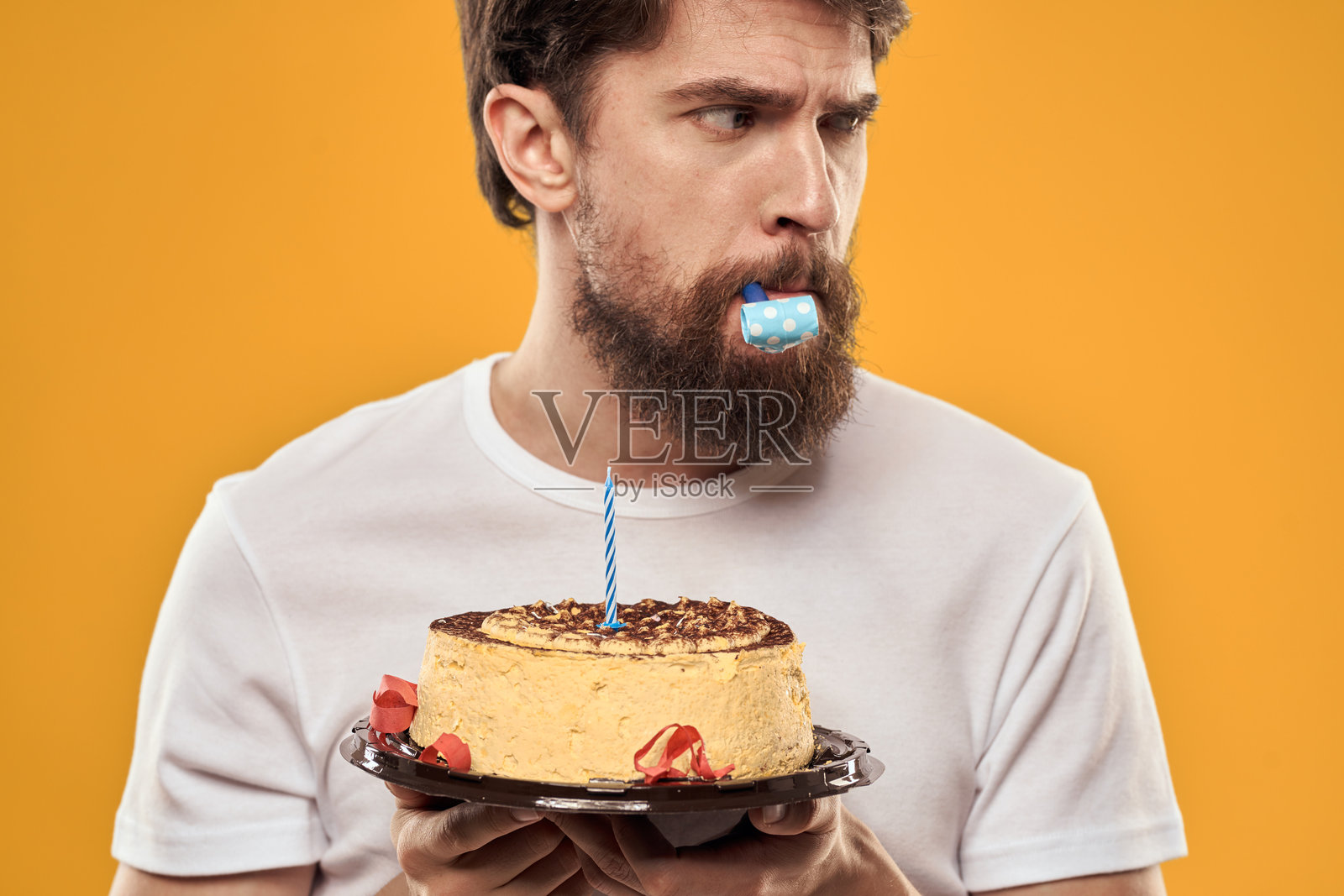 一个戴着帽子、留着胡子的男人正在庆祝他的生日，手里拿着蛋糕。照片摄影图片