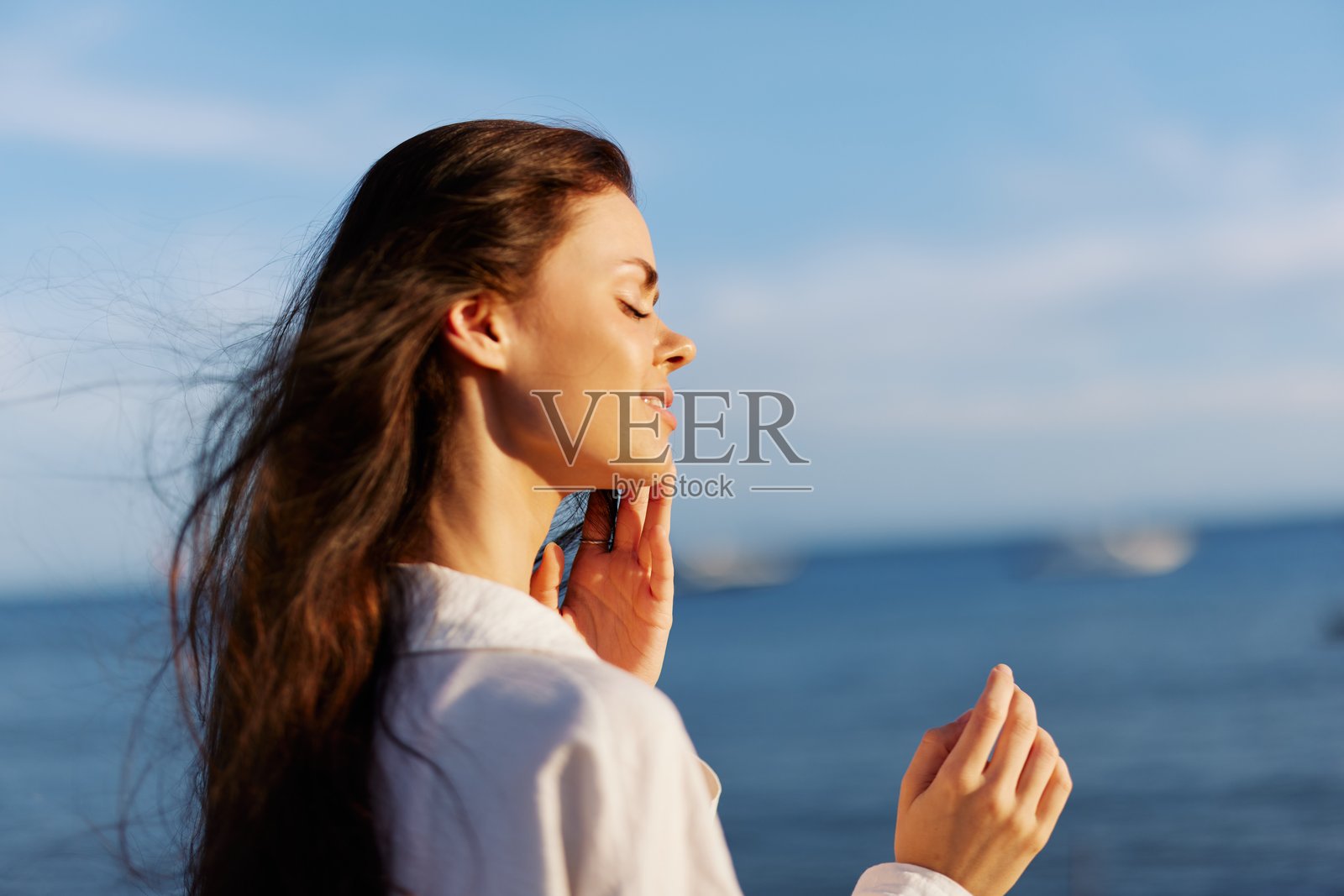 在巴厘岛的海滩上，女人在日落时分微笑着露出洁白的牙齿，享受自由的假期，快乐的旅行，夕阳的光辉，飞扬的秀发，阳光下的肌肤和头发护理理念。照片摄影图片