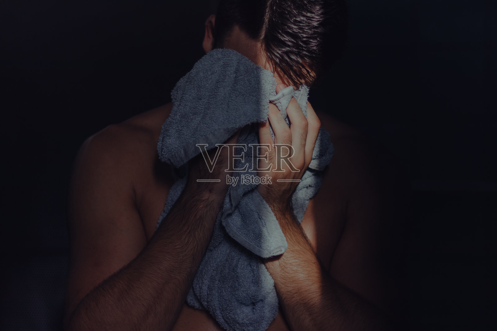 赤裸上身的男子在暗室中用毛巾遮住脸部照片摄影图片