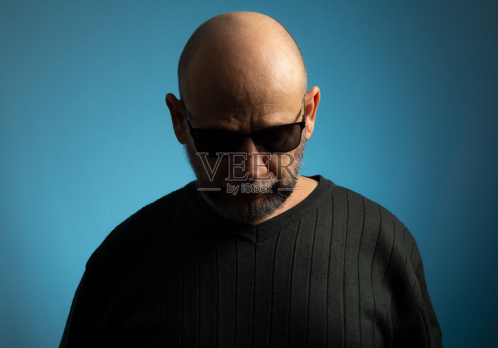 一个秃顶、蓄着胡子、戴着墨镜向下看的成熟男人的肖像。照片摄影图片