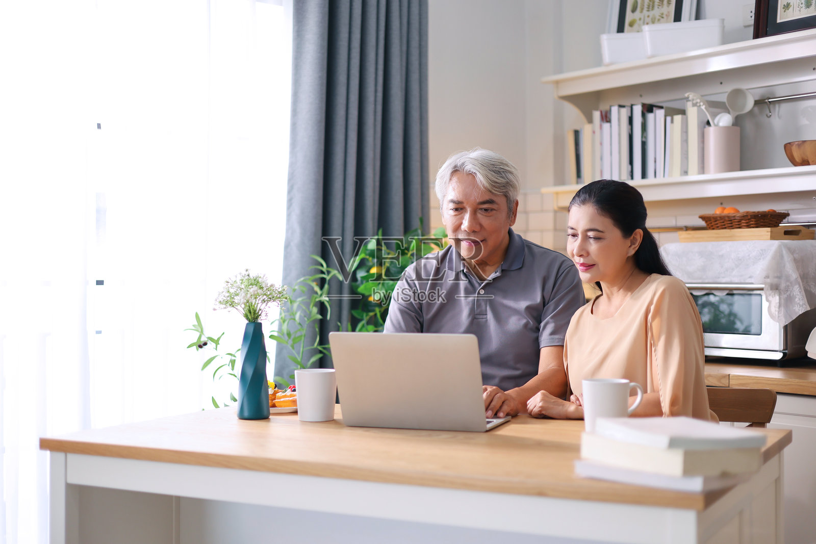 一位老年男子和他的妻子在厨房使用笔记本电脑观看烹饪视频。照片摄影图片