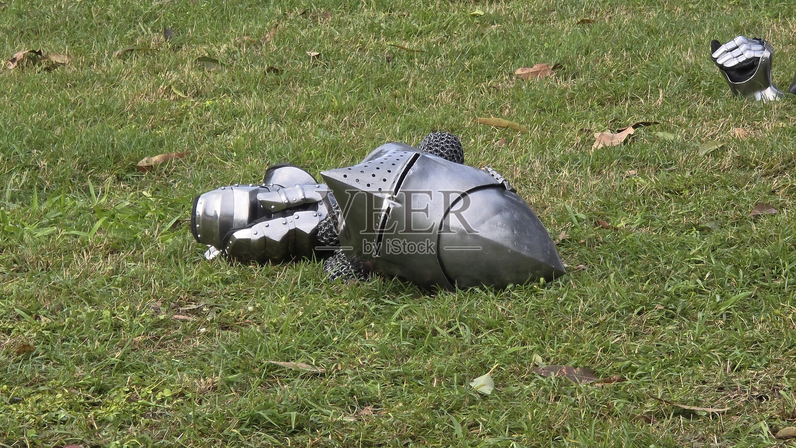 中世纪的钢盔和护手 resting on grass，暗示着历史重演或展示。链甲和精细的盔甲部件唤起了骑士装备的形象。照片摄影图片