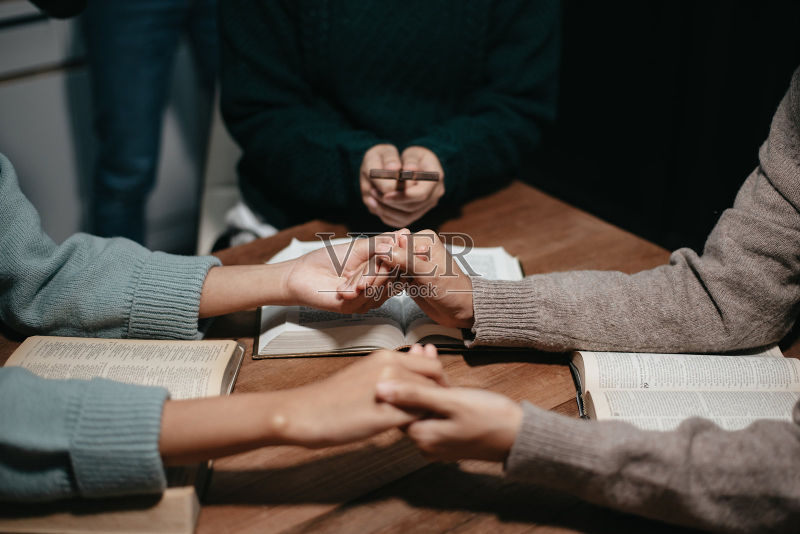一群基督徒围坐在木桌旁祈祷，模糊的圣经翻开的页面在他们的教室中。照片摄影图片