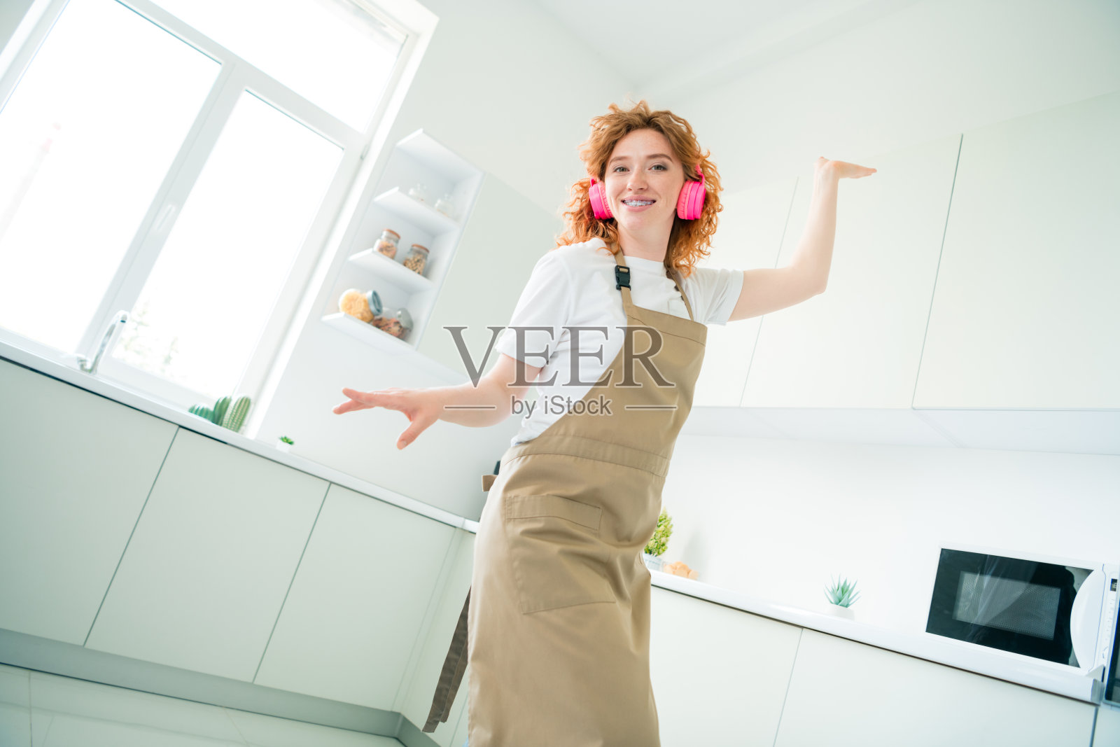 年轻女性在厨房里快乐地跳舞，穿着围裙和耳机，表达着快乐和积极的情绪照片摄影图片