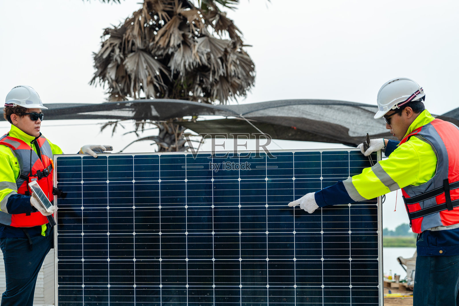工程师们检查光伏电池板模块。工业可再生能源的绿色电力。工人在现场准备材料，背景是堆放的面板。照片摄影图片