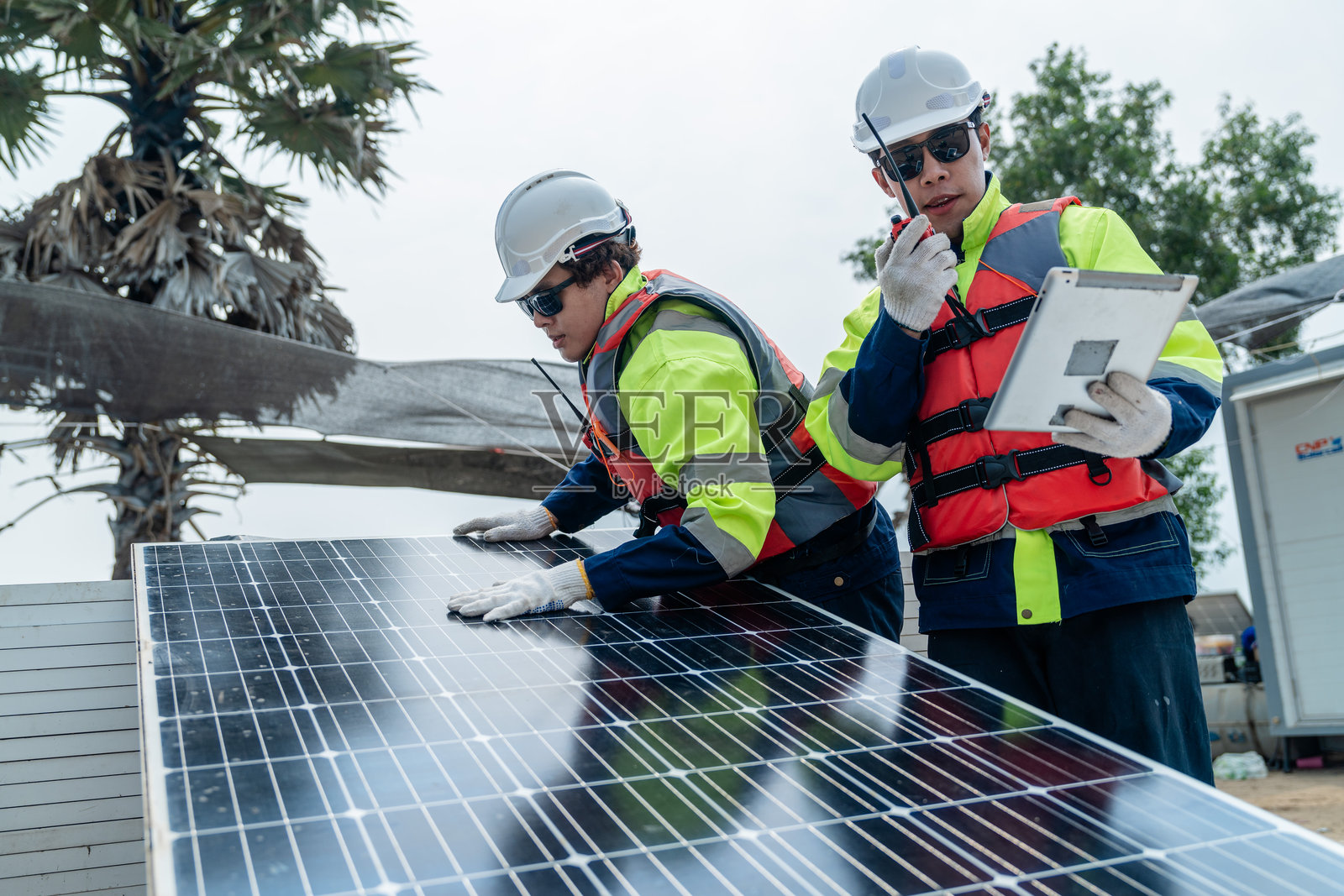 工程师们检查光伏电池板模块。工业可再生能源的绿色电力。工人在现场准备材料，背景是堆放的电池板。照片摄影图片