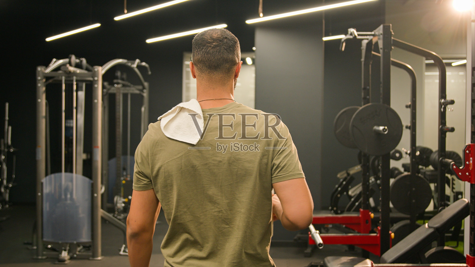 背影的非裔美国男性运动员教练，肌肉发达，肩上搭着毛巾，走出健身房，刚刚锻炼完，正在喝水。照片摄影图片