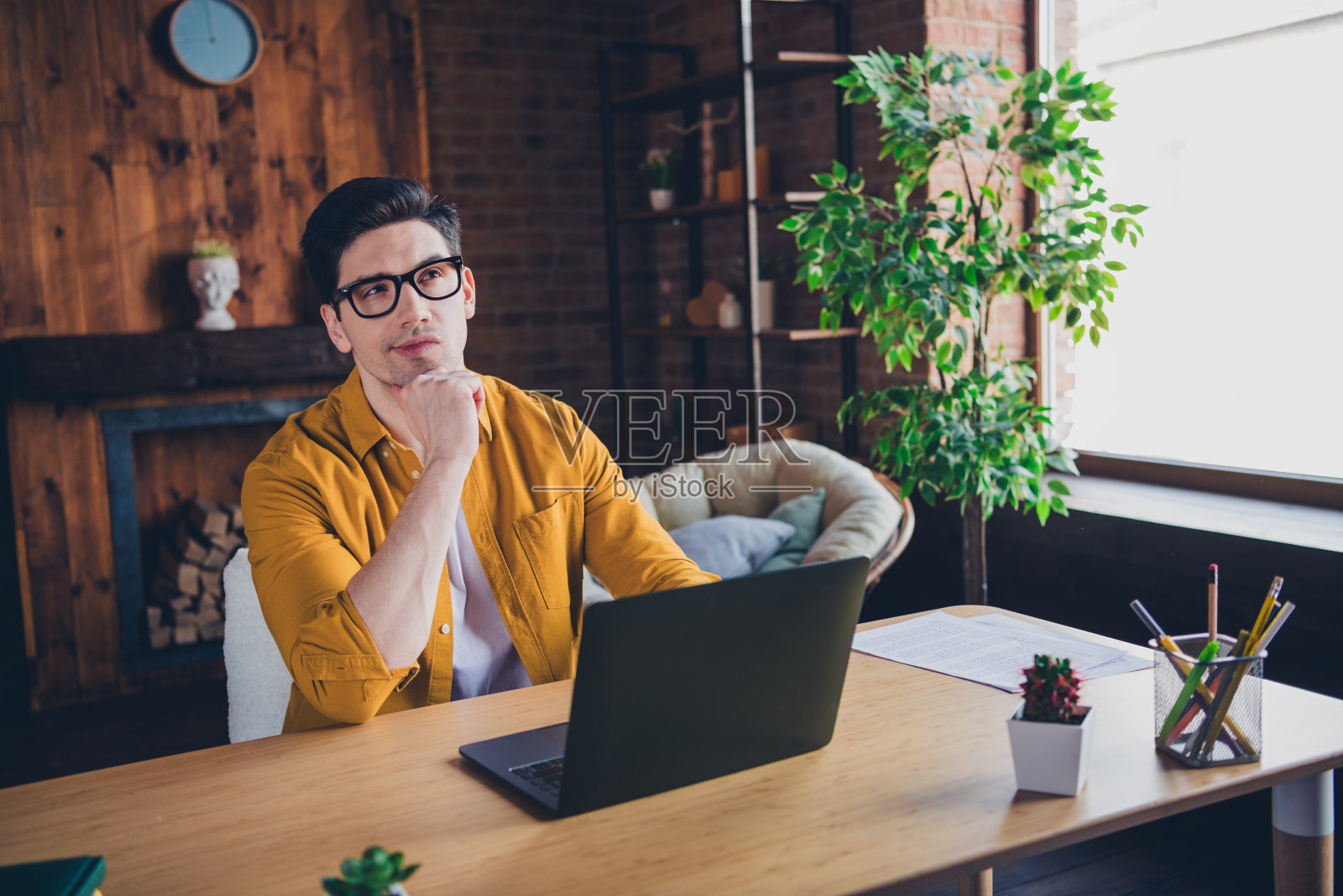 年轻男子穿着休闲风格，在明亮的阁楼环境中享受轻松的居家日，使用笔记本电脑工作。照片摄影图片
