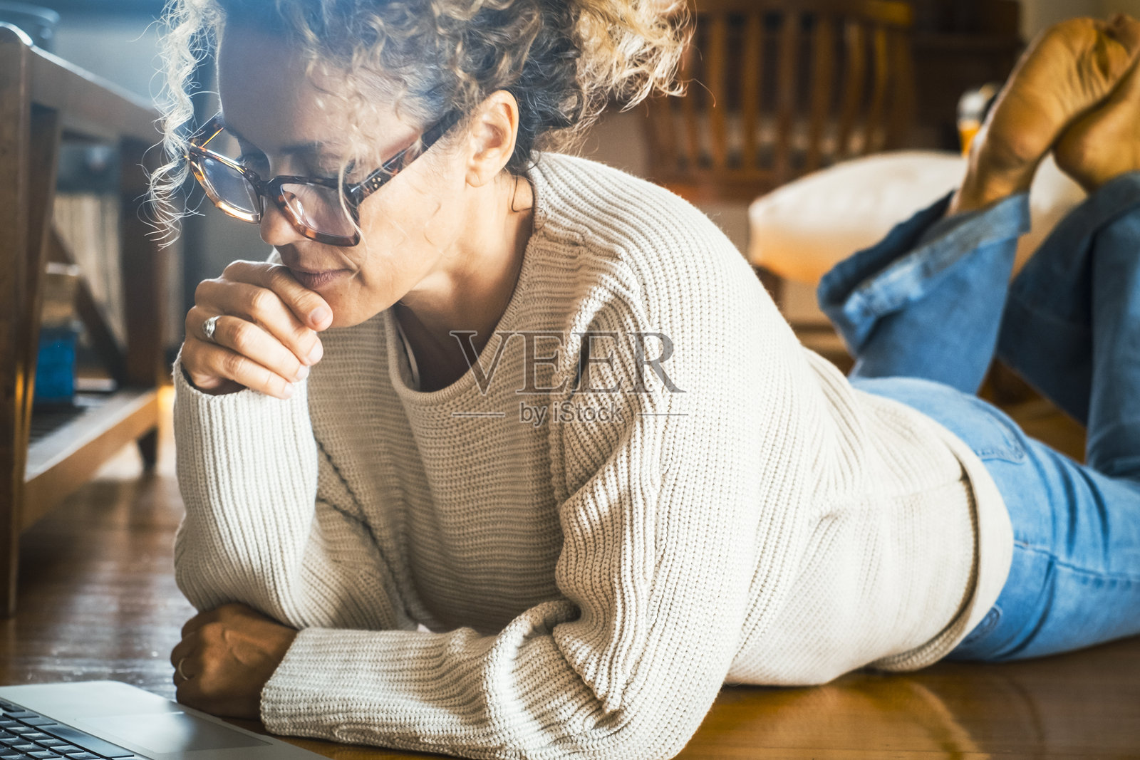 一个全神贯注的女人在家里使用笔记本电脑，独自躺在地板上。银行账户管理、网上购物或恋爱关系网上休闲活动的女性。无线电脑工作照片摄影图片