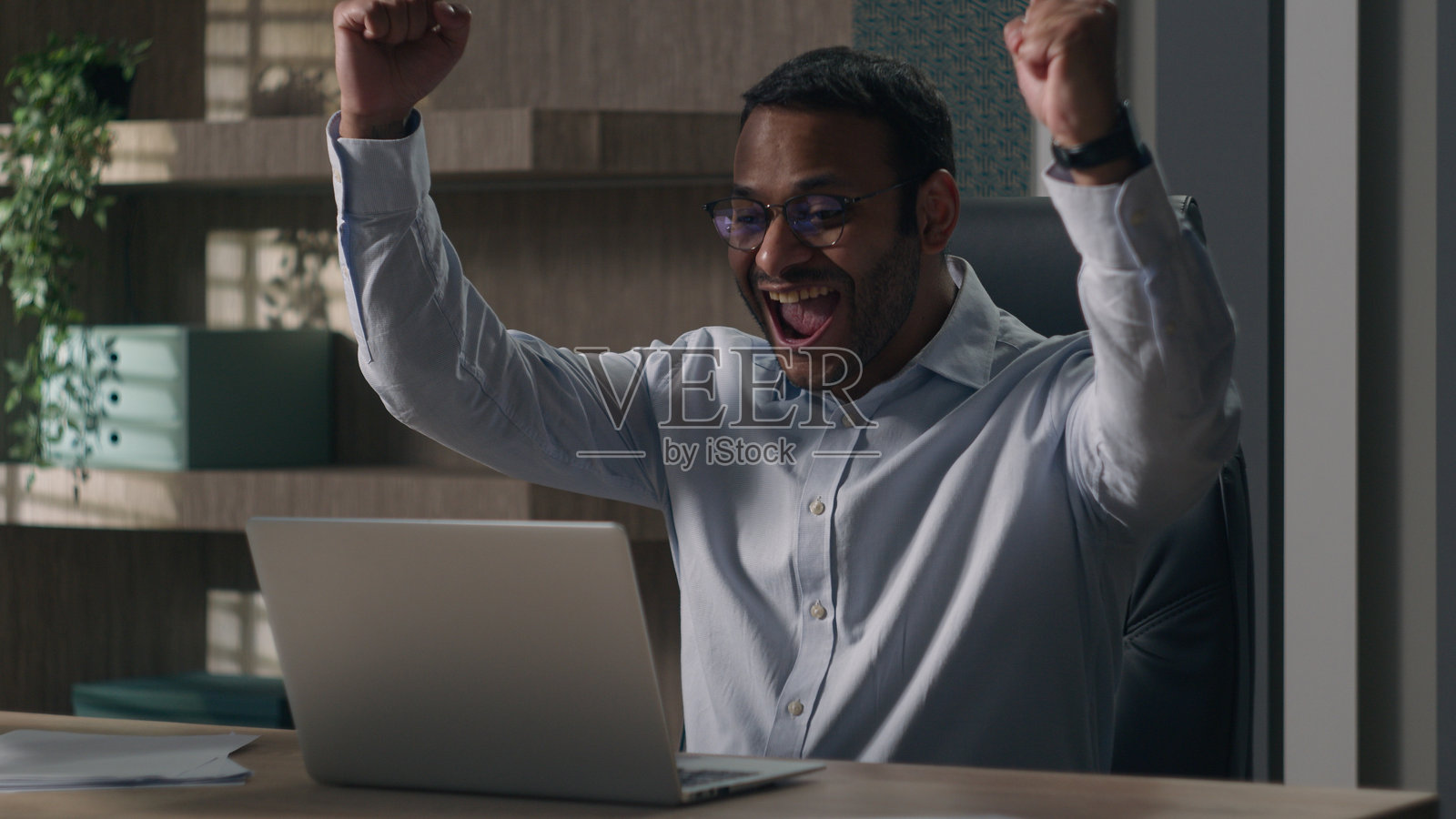 兴奋的印度商人和美国男子在办公室庆祝通过电脑赢得赌注的好消息，情绪激动，感受到成功的喜悦。照片摄影图片