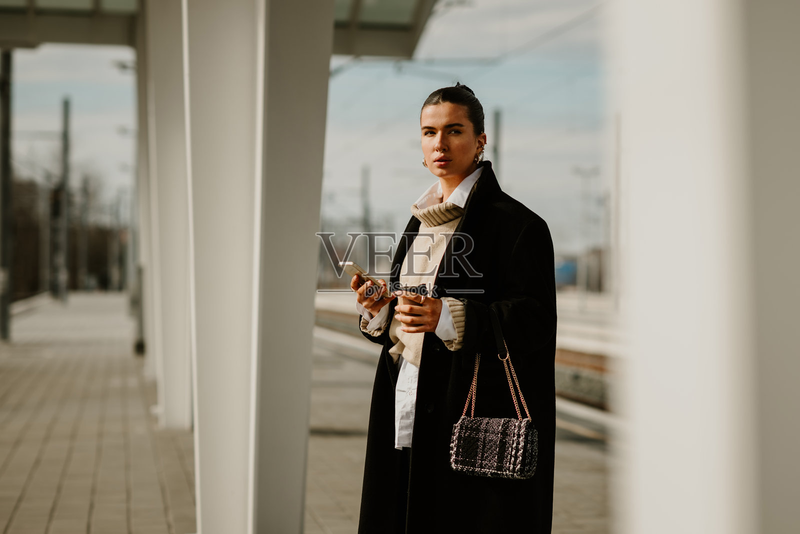 一个时髦的女人拿着手机在车站等火车。照片摄影图片