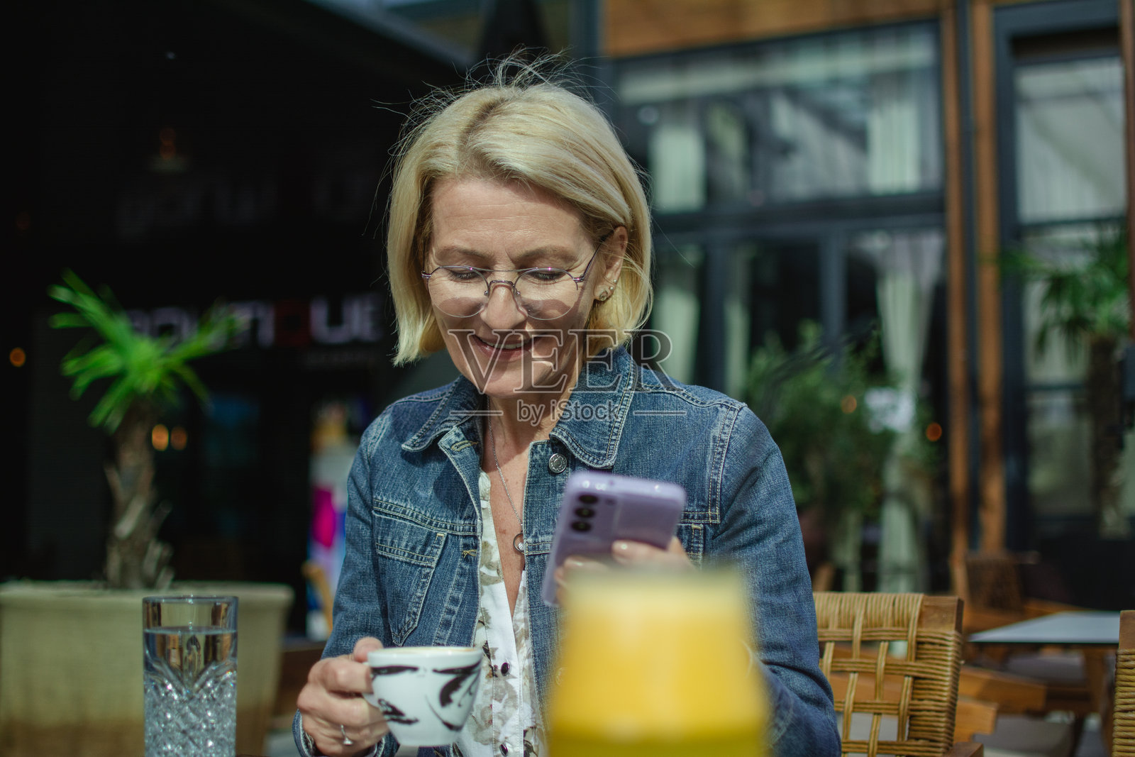 成熟的金发女子坐在外面的咖啡馆里，一边喝咖啡一边打电话照片摄影图片