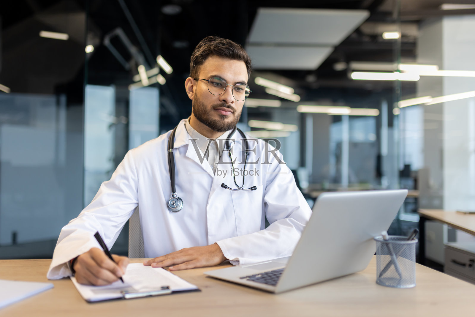 自信的男性医生在现代办公室里使用笔记本电脑工作照片摄影图片
