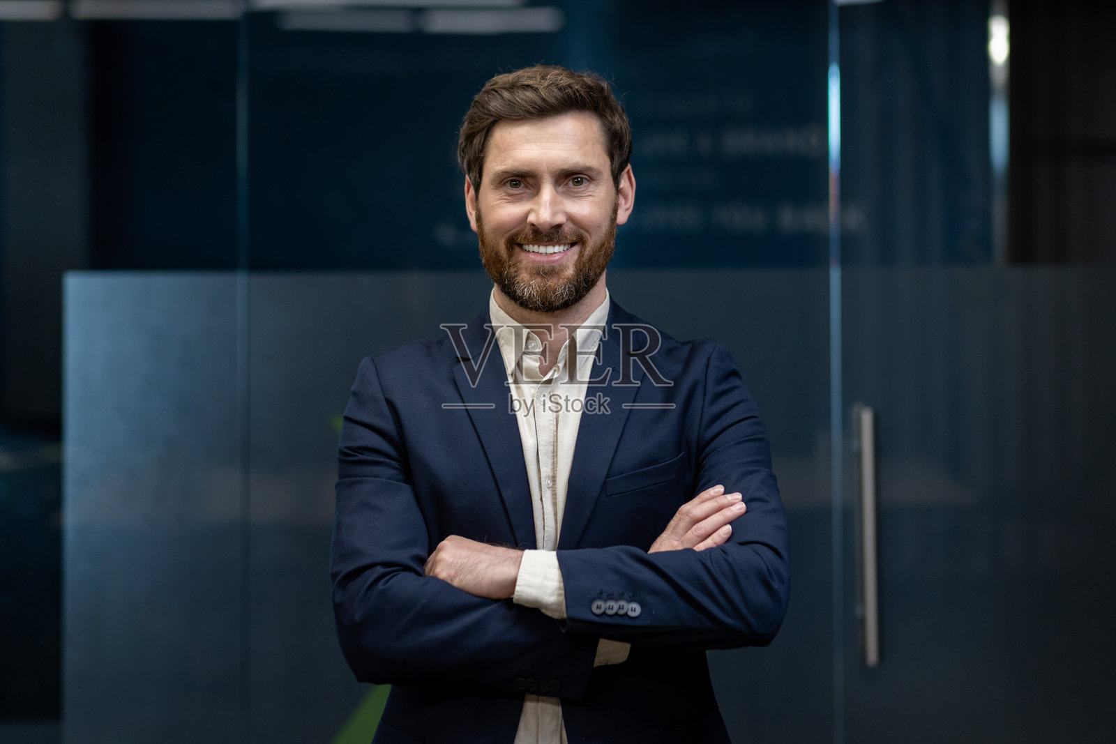 一位年轻的商务人士在办公室里打着哈欠，双臂交叉在胸前，自信地微笑着看向镜头。照片摄影图片