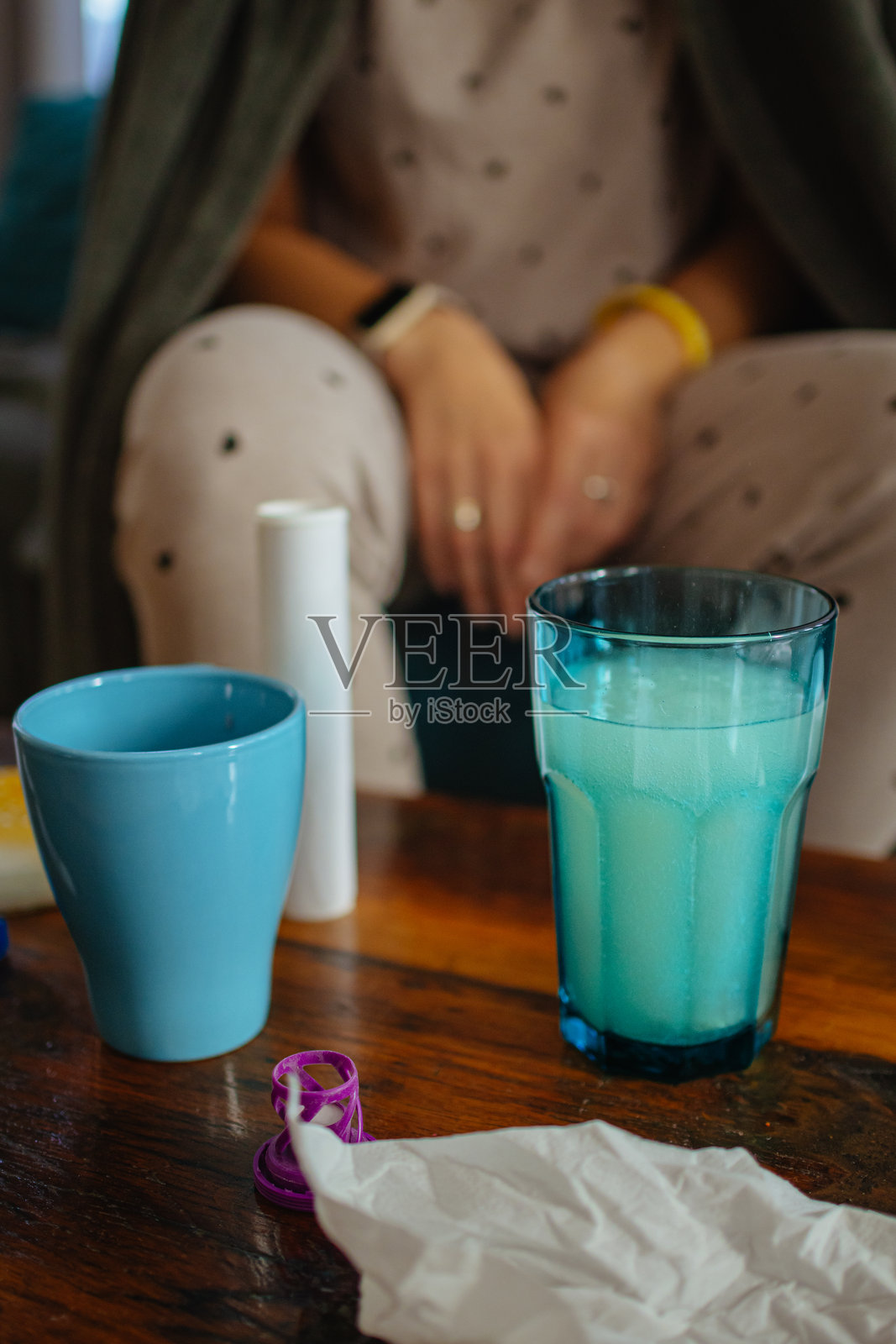 玻璃杯中的泡腾片。感冒、发烧、头痛和流感症状。生病的女人裹着毯子坐在客厅的沙发上。季节性呼吸道疾病。桌子上有温度计、药片、维生素和一杯水。照片摄影图片